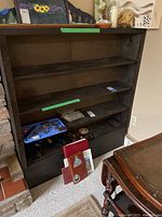 Front view of the wooden bookcase, showing three fixed shelves and some miscellaneous items around it (not included).