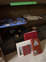 Photo showing red yearbook, folders, leather-cover notebook with military insignia stickers, and field dressing kits on shelves.