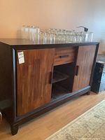 Front view of buffet cabinet showing two sliding doors, center drawer and open shelves on wooden floor with glass jars on top.