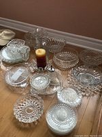 Overall view of assorted crystal and glass bowls, trays, and water pitcher laid out on the floor, showing variety of patterns and shapes.