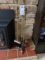 Full view of the brass fireplace tool set with stand positioned on tiled hearth, showing poker, shovel, and broom.