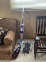 Photo showing Thane H2O Mop steam cleaner upright beside a sofa and two handheld vacuums on floor next to a chair.