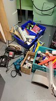Overview of boxed hardware items, hand tools, power tools on basement floor