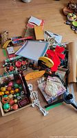 Overview of assorted holiday decorations including Christmas ornaments, Halloween skeleton decoration, tree stand, wrapping paper, and boxed games on a wood floor.