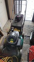 Top view of Yardworks lawn mower with black mulch bag and handlebar in indoor shed.