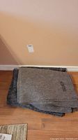 Two gray felt moving blankets folded, showing DND/MDN embroidered lettering on one.
