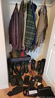 Photo showing five jackets hanging in a closet and four pairs of boots along with several black gloves and a small grooming device on the floor below.