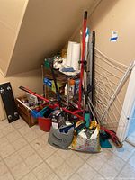 Metal wire shelving and miscellaneous cleaning supplies arranged under staircase, mop, bucket, drying rack, Swiffer mop, and broom set visible