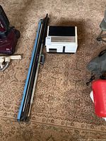 Photo showing Paximat 2000 slide projector next to the rolled projection screen on patterned carpet