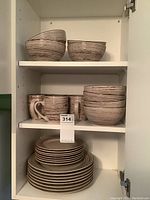 Shelves showing stacked stoneware dinner plates on bottom, luncheon plates in middle with stoneware cups, and stoneware bowls on top. All pieces have a horizontal striped pattern in earth tones.
