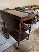 Side-angle view of the vintage tea wagon showing the spoked wheels, turned legs, and drop-leaf sides folded down.