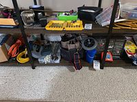 Photo of shelving unit bottom shelves showing socket and bit set, tool bag, caddies, extension cords, and various hardware items