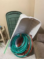 Photo of large white Rubbermaid tote with green lid removed, containing two coiled garden hoses, one green and one brown.