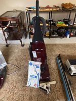 Front view of the Samsung Quiet Jet vacuum cleaner with vacuum bags and two mismatched attachments in front on the floor.