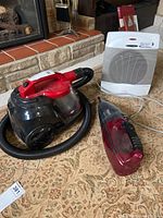 Bissell Zing vacuum with hose, Shark cordless handheld vacuum, and Sunbeam heater placed on carpet near fireplace