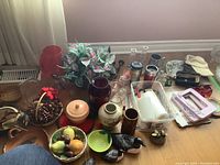 Overview of vases, ceramic items, baskets with decorative pine cones, artificial fruit, ball caps, candles, beer steins, and loon family figurines on the floor near a wall.