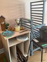 Image of multiple home decor items including blue painted table with LP storage, wind chimes in the storage area, metal wastebasket, black plastic stool, and metal plant stand.