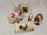 All items arranged including two white wooden roosters, ceramic turkey pieces, glass chicken, two rooster plates, and metal plate stand.