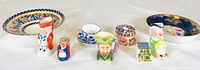 Photo showing four Toby jugs, two decorative plates, and three miniature tea accessories arranged on a white surface