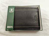 Roots black leather wallet in original green box with visible 'Roots' logo and maple leaf symbol
