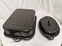Two black speckled oven roasting pans with lids, one rectangular and one oval-shaped, shown side by side
