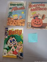 Photo of three vintage comic books: two Dennis the Menace and one Betty, all in plastic sleeves with colorful illustrated covers.