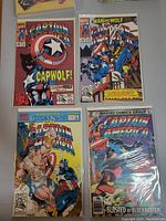 Four Captain America comics laid out, each in a protective plastic sleeve, showing front covers with colorful artwork.