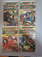 Photo of four Captain America and Falcon comic books, arranged in two rows, showing front covers with colorful action scenes and text