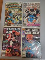 Photo of four Captain America comic books front cover view featuring colorful action covers and titles, protected in plastic sleeves.
