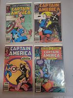 Photo showing four Captain America comic books arranged in grid, covers visible with varying action scenes and comic titles.