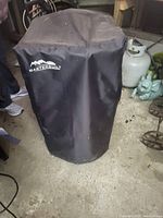 Masterbuilt electric smoker covered with black protective cover.