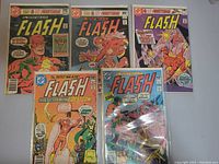 Five Flash comic books laid out in plastic sleeves showing covers with various characters and action scenes.