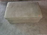 View of beige storage ottoman showing fabric exterior and cushion top