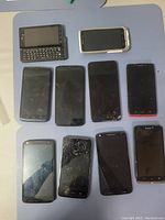 Ten Motorola phones arranged on a blue surface, including two slide-out keyboard phones and multiple touchscreen smartphones, some with cracked screens.