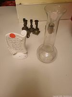 Assorted items on a countertop including a tall clear glass vase, white ceramic plaque with text, and metal candlesticks.