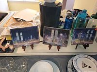 Front view of three out of four decorative rectangular plates depicting the New York City skyline including the Twin Towers, showing nighttime cityscape.