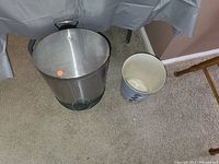 Stainless steel pedal trash can and small white plastic trash bin on carpeted floor