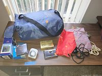 Blue pack and play bag with small household items spread on a table including a thermostat timer, cassette case, and small pouches