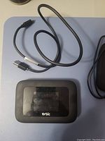 Orbic branded mobile hotspot with USB charging cable visible on blue mat surface.