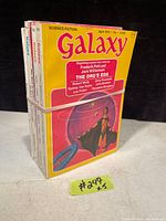 Stack of five Galaxy science fiction magazines showing worn yellow cover and scifi illustration on front magazine dated April 1974 with highlighted story title 'The Org's Egg' by Frederik Pohl and Jack Williamson.