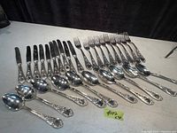 30 pieces of vintage sterling silver cutlery laid out flat on a surface: 10 knives, 10 forks, 10 soups spoons all with patterned handles.