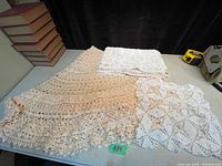 Photo showing crochet table runner and folded round table cloth side by side on grey surface, displaying lace and ruffled details