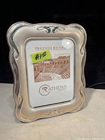 Front view of sterling silver picture frame with decorative curved edges and scroll embellishments, containing a placeholder image marked Preziosi Ricordi and Athena Argento.