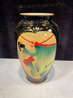 Front view of the vase showing a painted Asian figure in traditional dress with red sash, black background and gold floral accents.