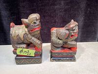 Photo showing two hand carved wooden book ends depicting lion-like mythical creatures, painted with red, black, and natural wood tones.