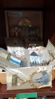 Photo showing part of the bookmarks in packaging arranged in a wooden case with other items, highlighting the metal bookmark with clock tower design in front.