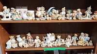 Wide view of two shelves filled with numerous Cherished Teddies figurines placed side by side, showing variety and number of pieces in collection.