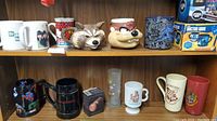 Front view showing mugs from Breaking Bad, Scooby-Doo, Rocket Raccoon, Taz, Disney, Beatles, and Game of Thrones grouped on shelf.