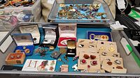 Photo showing a collection of cufflinks and tie pins arranged on a blue tray and surface in boxes and loose