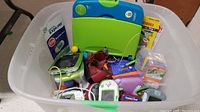 Large bin filled with multiple LeapFrog and VTech electronic educational games and accessories, showing a variety of consoles and cartridges.
